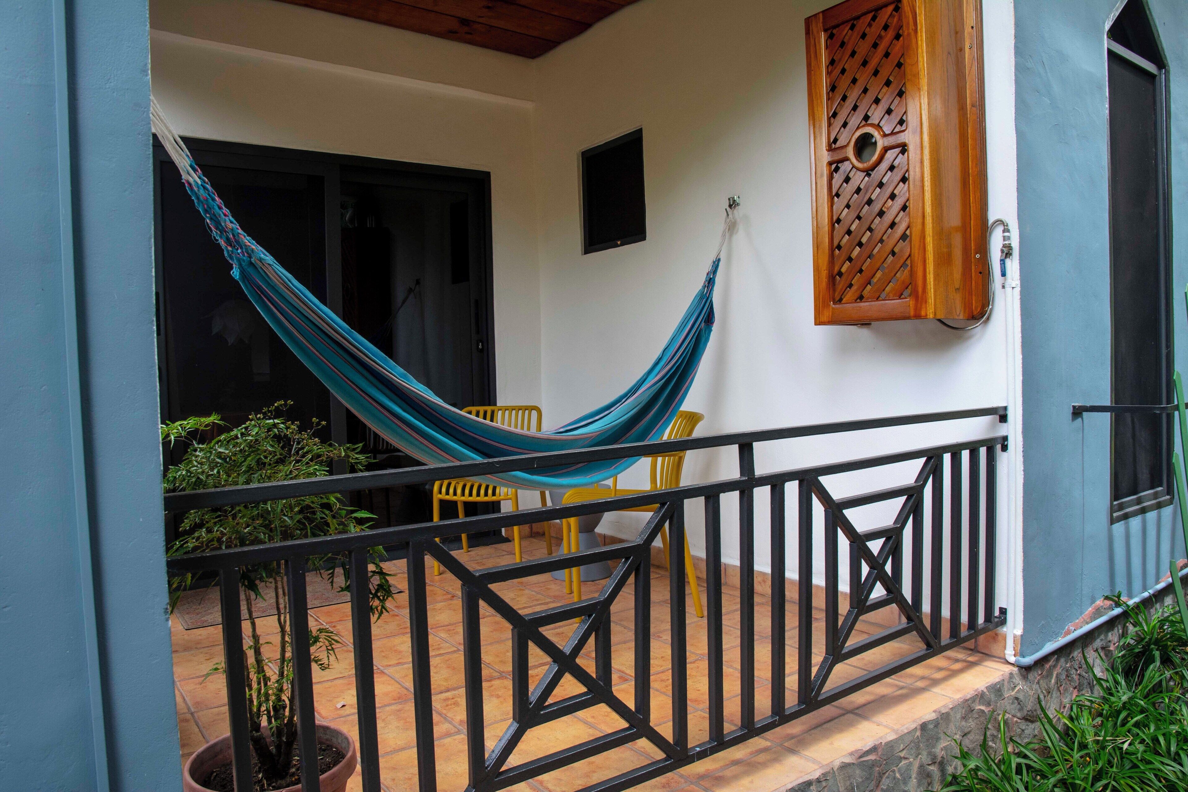 A balcony with a hammock, yellow chairs, and a potted plant.