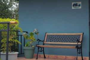 Un banco con respaldo de celosía y listones de madera, ubicado frente a una pared azul con un letrero 'Sark'.