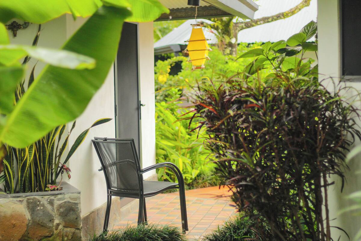 A covered outdoor seating area with a chair, potted plants, and a hanging light fixture.