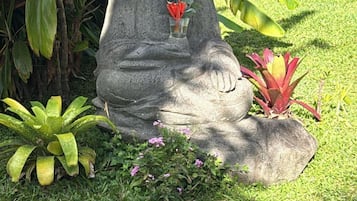 A statue of a seated figure holding a flower, surrounded by lush greenery and a tiled border.