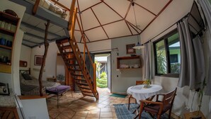A room with a wooden staircase, a bed, a table with chairs, a fan, and a window with curtains. - Hotel Isla Verde (Boquete)