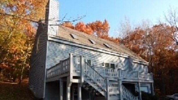 A small, single-story building with a steeply pitched roof and a small porch with a staircase. - House on Pond Court (Galena)
