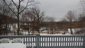 A snow-covered outdoor area with a table and chairs, a fence, and leafless trees. - House on Pond Court (Galena)