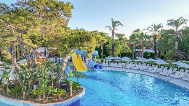A swimming pool with a water slide, surrounded by palm trees and lounge chairs. - Catamaran Quality Times - All Inclusive (Kemer)