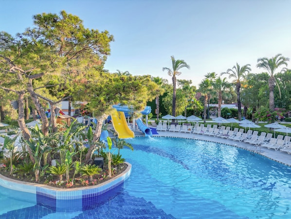 A swimming pool with a water slide, surrounded by palm trees and lounge chairs. - Catamaran Quality Times - All Inclusive (Kemer)