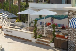 Un café avec une terrasse, des parasols blancs et un mur décoré sur le thème des vagues.