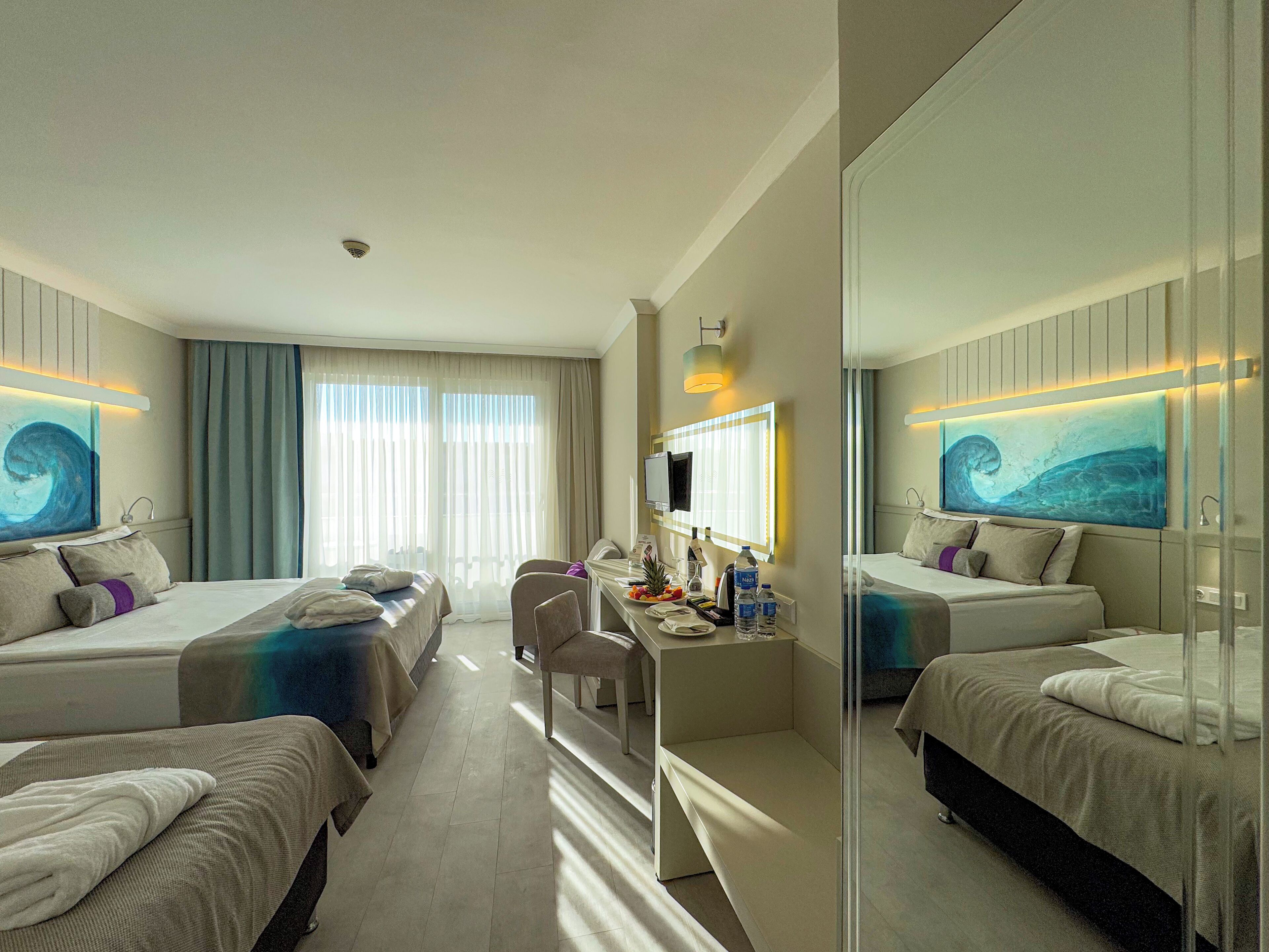 A hotel room with two beds, a desk with a chair, a TV, and artwork on the walls.