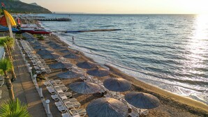 A beach with rows of sun loungers and thatched umbrellas, a pier extending into the sea, and a clear sky. - Catamaran Quality Times - All Inclusive (Kemer)