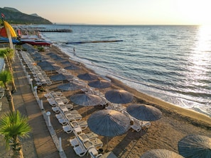 A beach with rows of sun loungers and thatched umbrellas, a pier extending into the sea, and a clear sky. - Catamaran Quality Times - All Inclusive (Kemer)