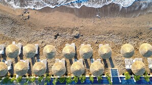 Une plage bordée de rangées de parasols et de chaises longues, une étendue de sable et des vagues qui se brisent sur le rivage.