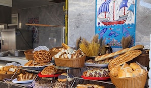 A variety of breads and pastries displayed in baskets and trays, with a decorative wall featuring a ship and sea creatures in the background. - Catamaran Quality Times - All Inclusive (Kemer)