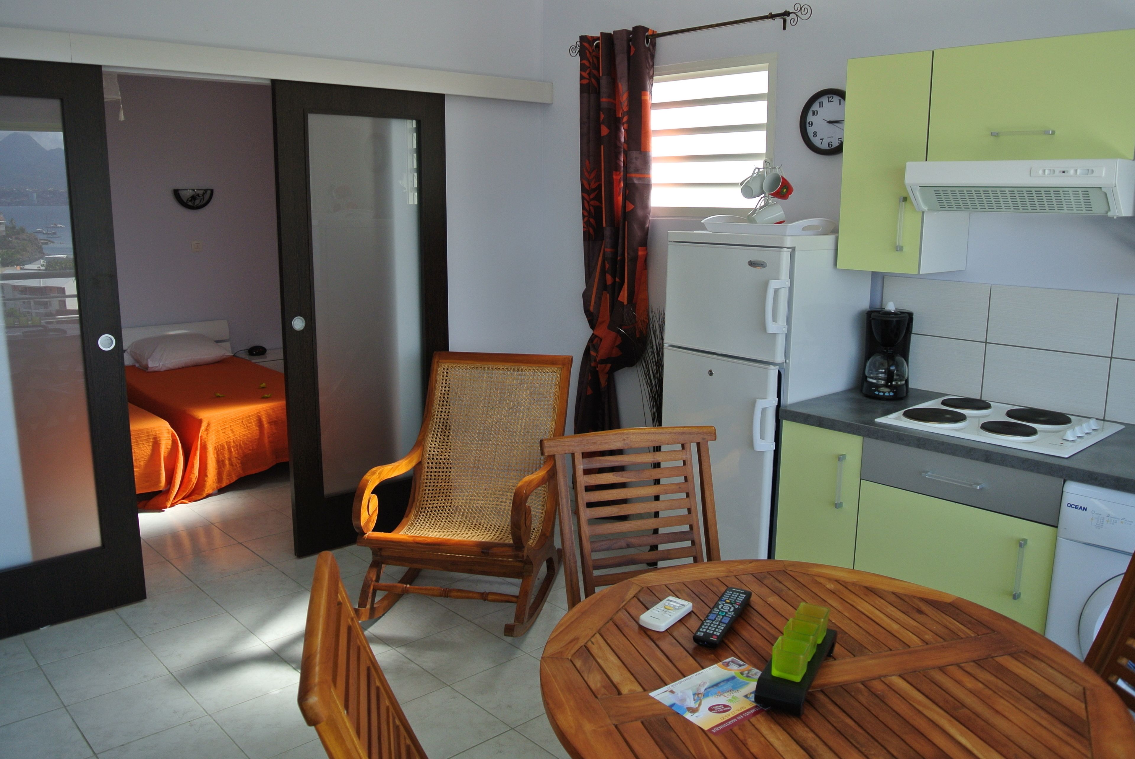 A compact hotel room with a bed, a dining table with chairs, a kitchenette, and a view of the city.
