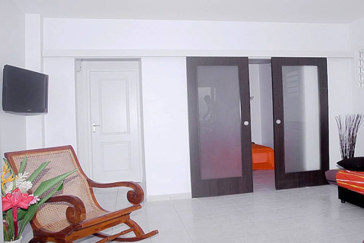 A living room with a sofa, a rocking chair, a flat-screen TV, and a door leading to another room.