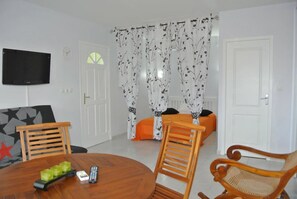 A living room with a wooden dining table, two wooden chairs, a television mounted on the wall, and a sofa with a star-patterned cushion. - Residence Villas Melissa (Trois-Ilets)