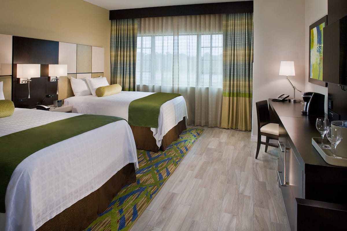 Une chambre d’hôtel avec deux lits, un bureau avec une chaise, une télévision et une fenêtre avec des rideaux.