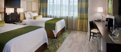 A hotel room with two beds, a desk with a chair, a television, and a window with curtains.