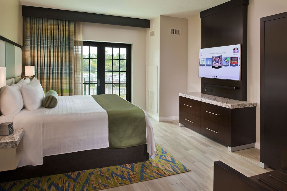 Une chambre d’hôtel avec un lit, une télévision, un bureau et une fenêtre avec des rideaux.