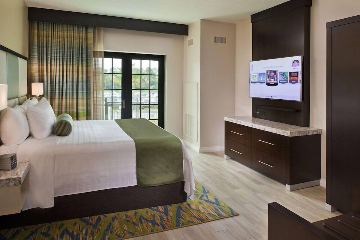 Une chambre d’hôtel avec un lit, une télévision, un bureau et une fenêtre avec des rideaux.