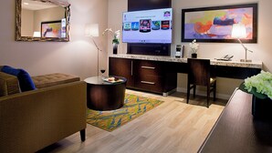Ein modernes Hotelzimmer mit einer Couch, einem Couchtisch, einem Fernseher, einem Schreibtisch und einem Sessel.