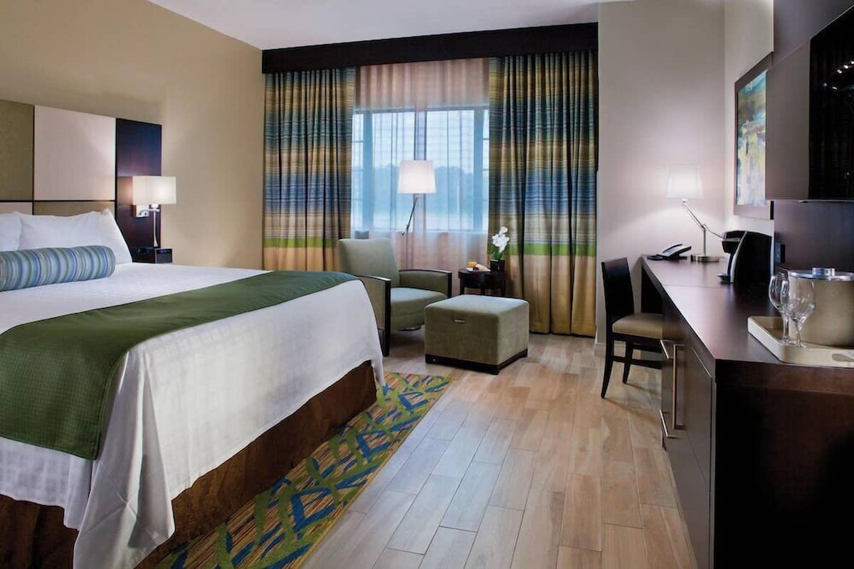 Une chambre d’hôtel avec un lit, un bureau, une chaise, une petite table et une fenêtre avec des rideaux.