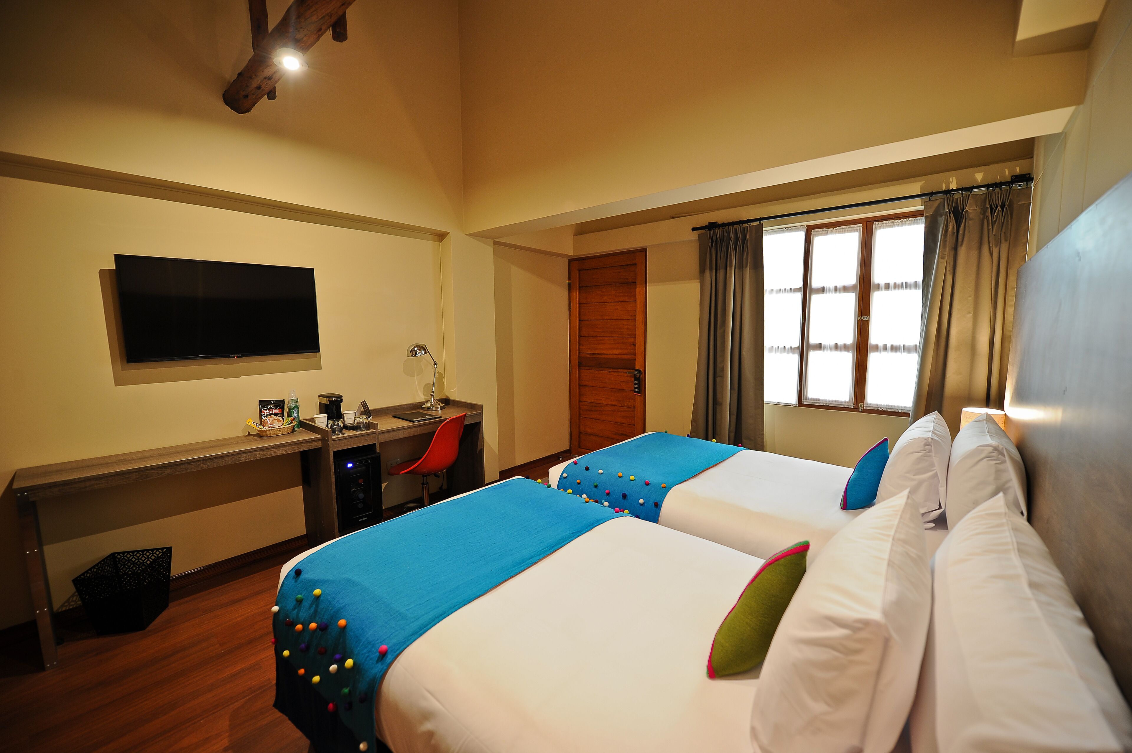 A hotel room with two beds, a desk with a chair, a TV, and a window with curtains.