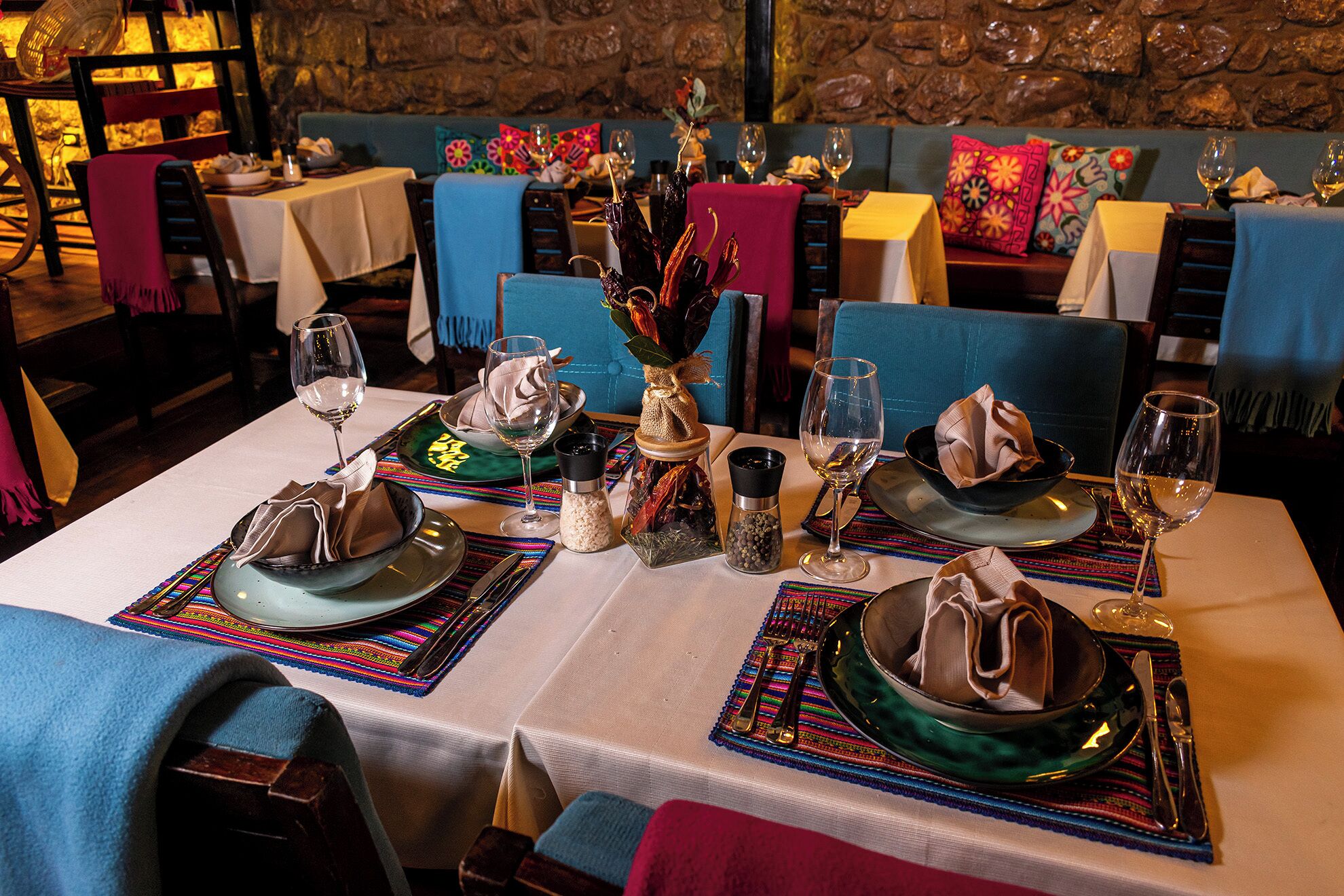 A restaurant setting with tables set for dining, featuring colorful table runners and traditional table settings.