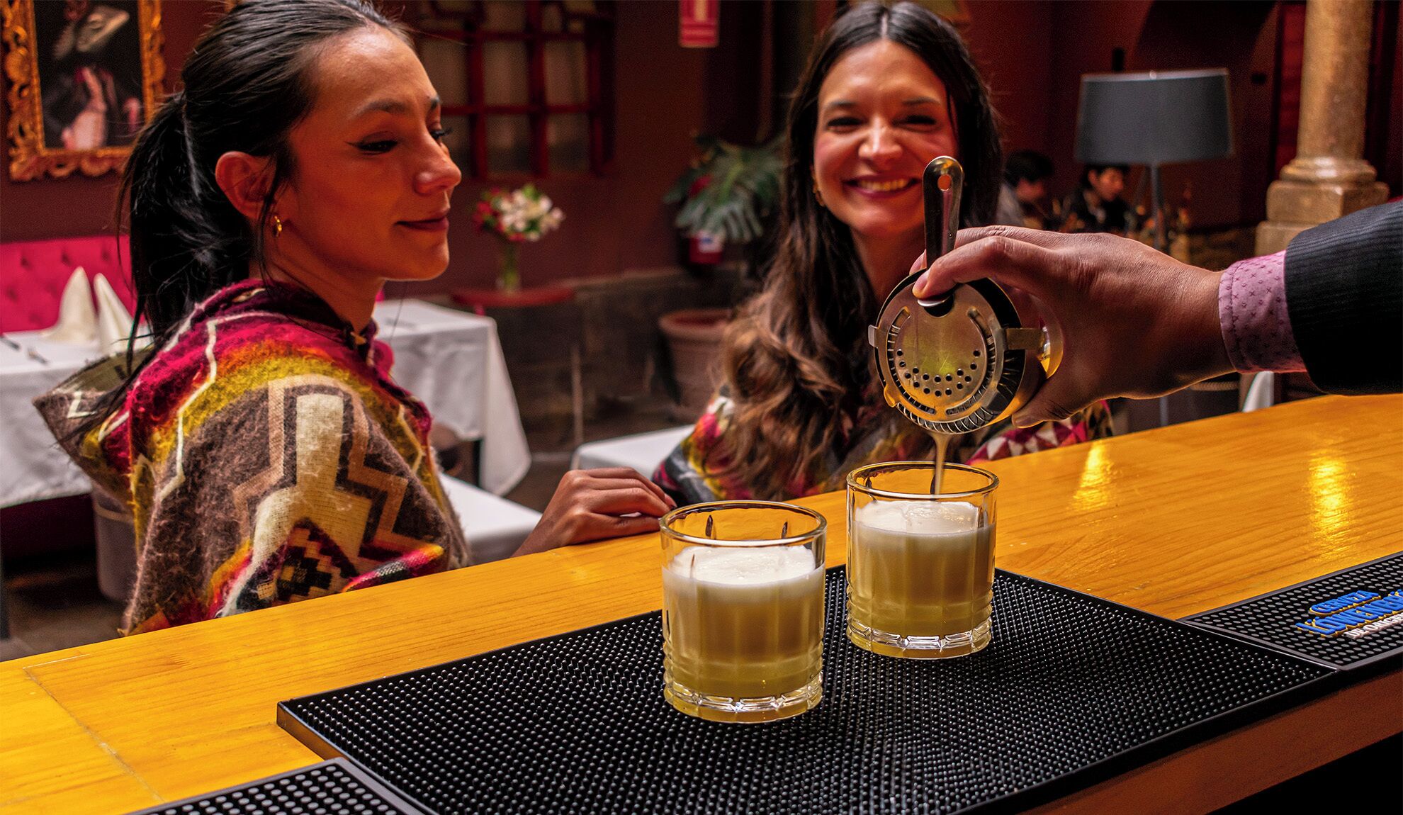 A bar setting with two glasses of beer on a black mat.