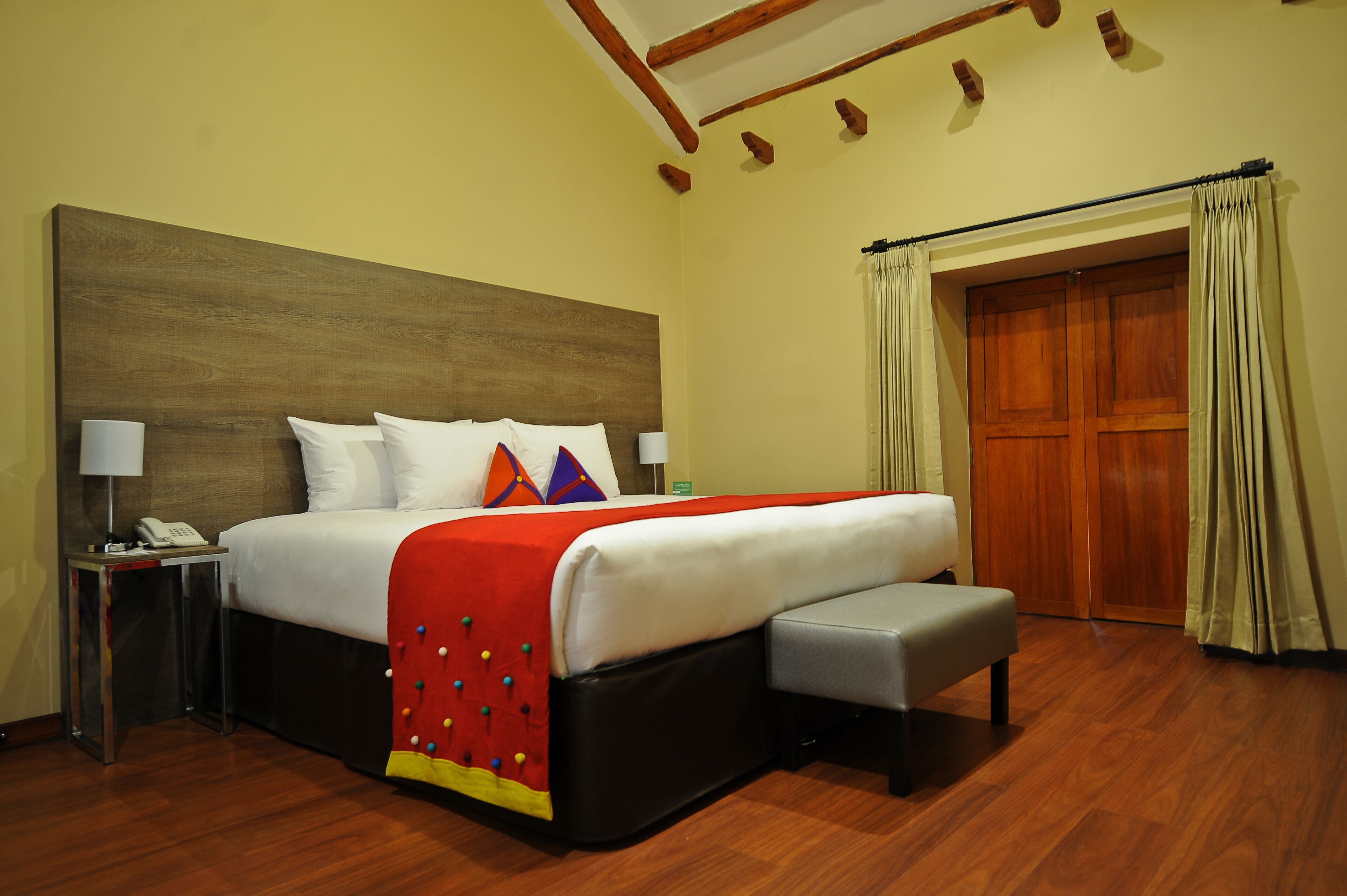 A hotel room with a large bed, a bedside table with a lamp, a wooden headboard, and a wooden wardrobe.