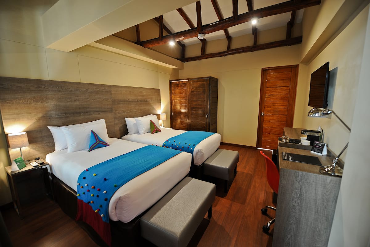 A hotel room with two beds, a desk, a chair, a wardrobe, and a mirror.