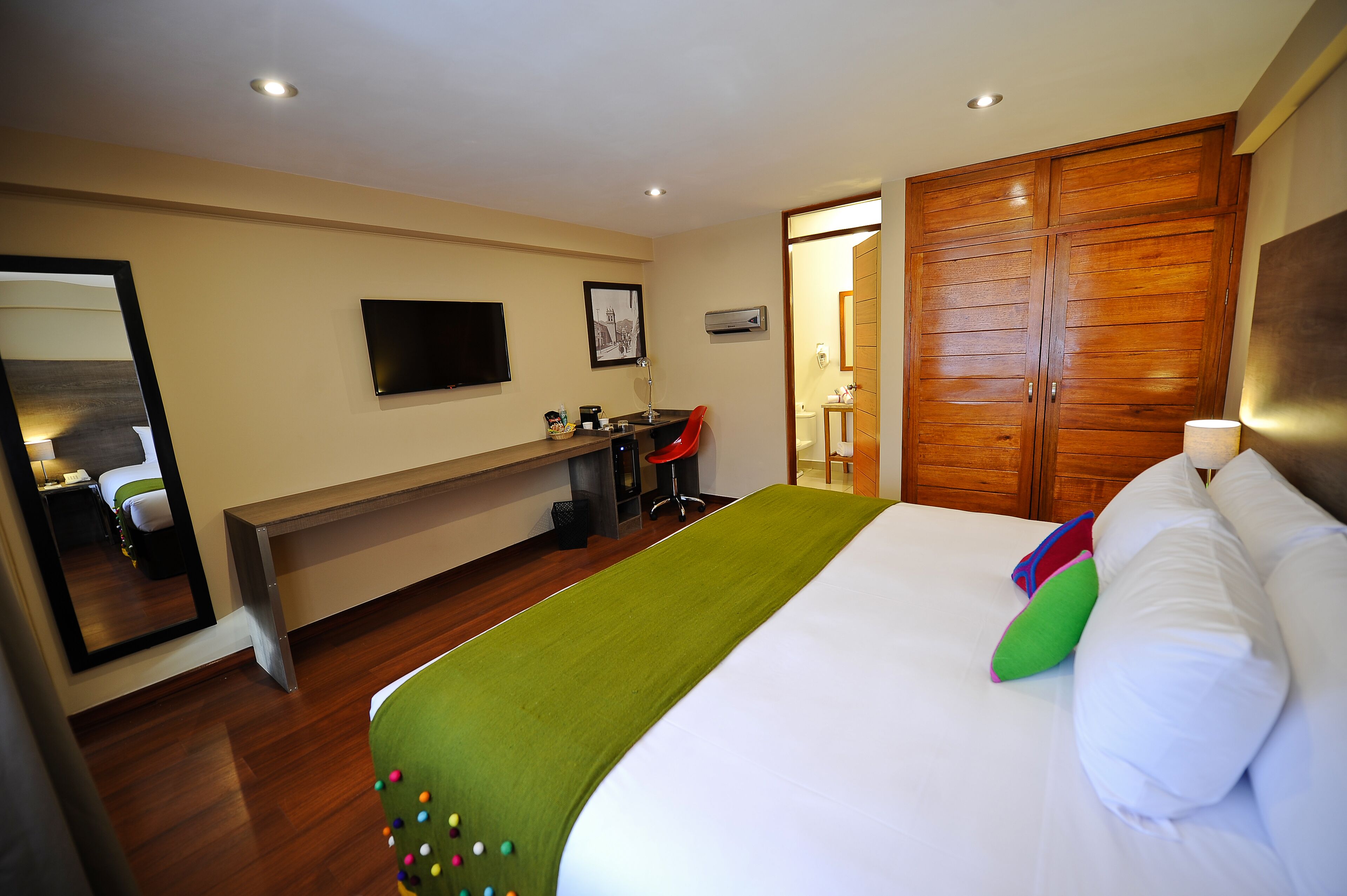 A hotel room with a bed, a desk, a chair, a mirror, and a wardrobe.