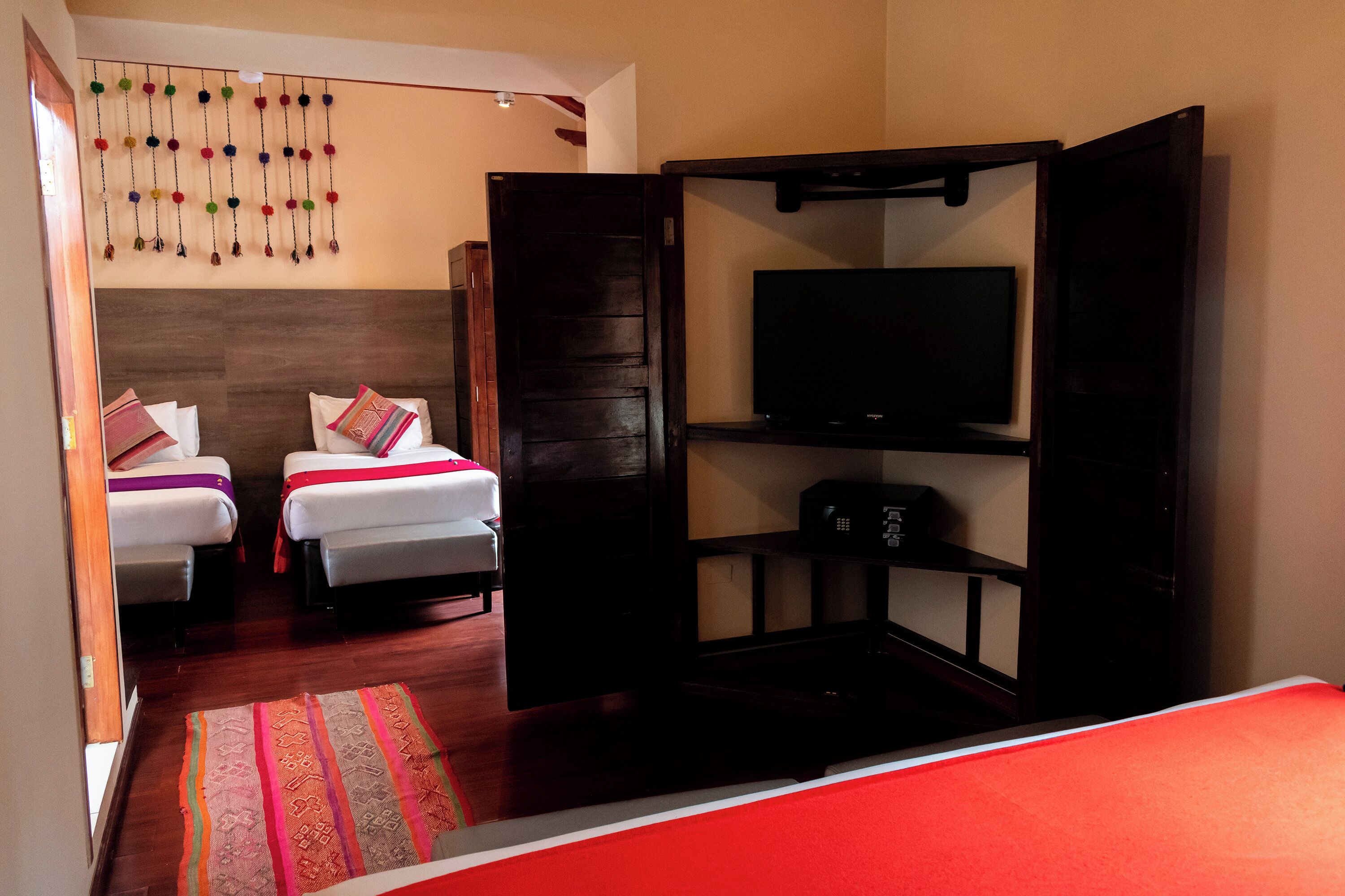 A hotel room with two beds, a TV, and a wooden wardrobe.