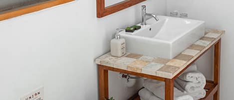 Un baño con un lavamanos blanco, tocador de madera, espejo con iluminación, inodoro y planta en maceta.