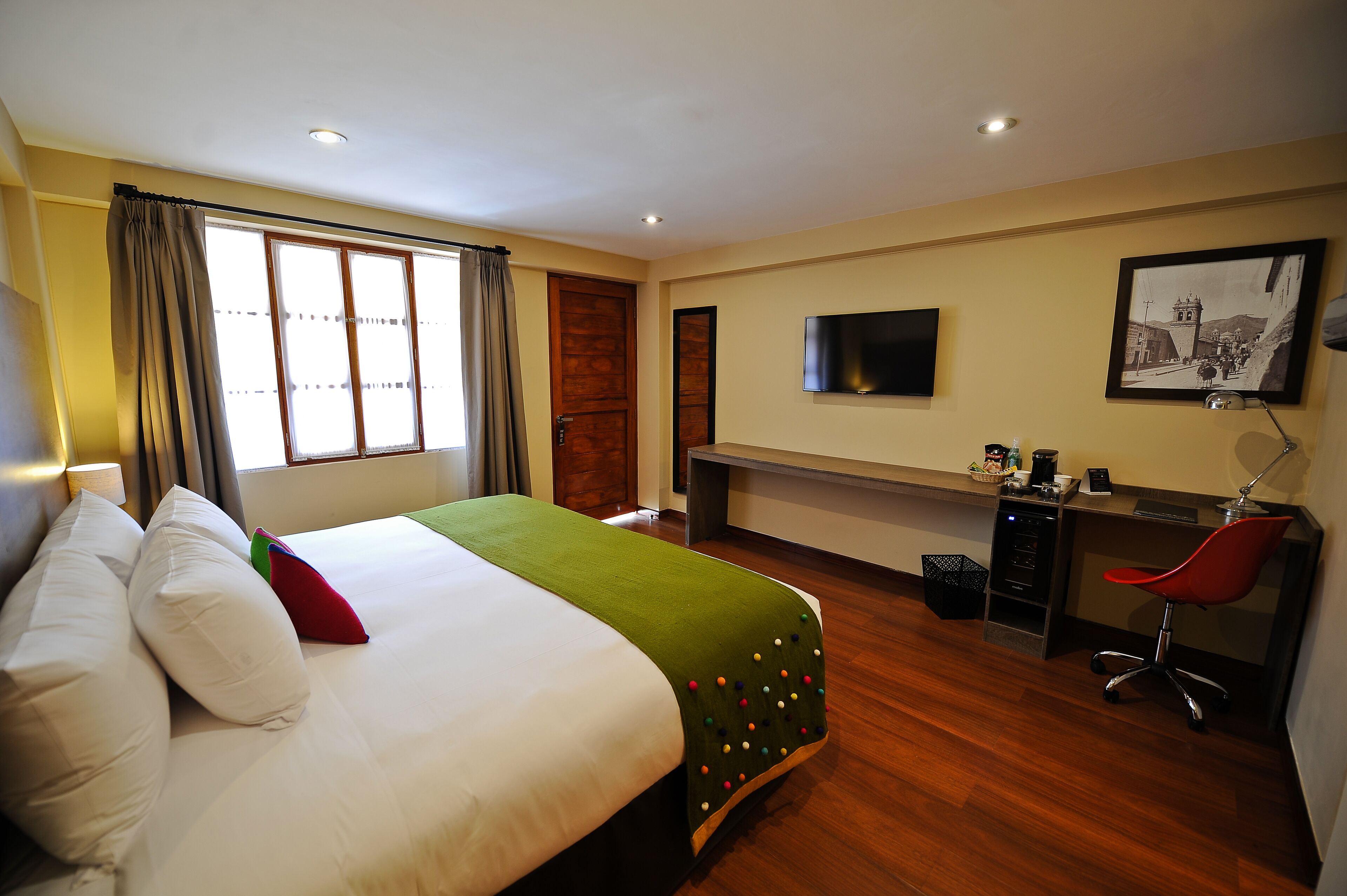 A hotel room with a bed, a desk, a chair, a TV, and a picture on the wall.