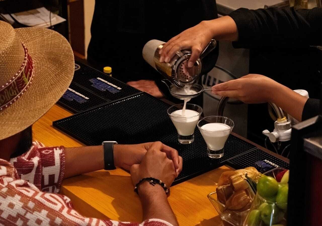 A person pouring a drink into a glass, with a laptop and a keyboard on the table.