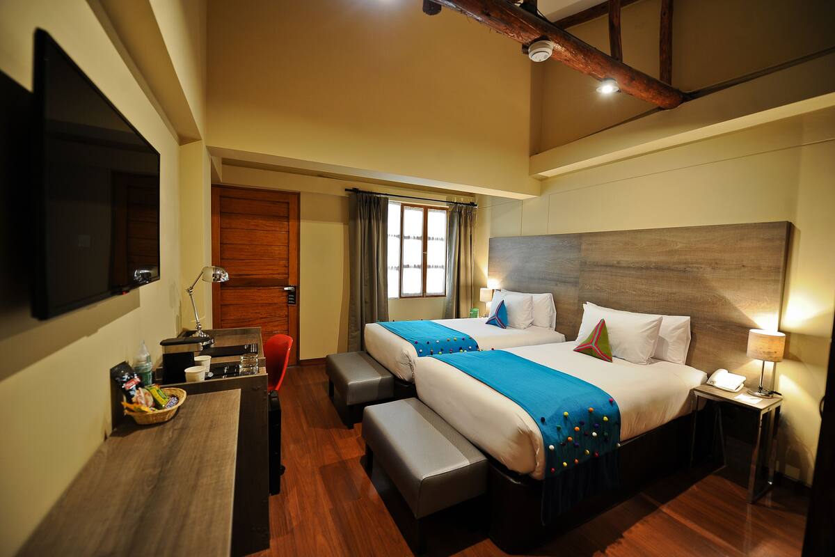 A hotel room with two beds, a desk, a chair, a TV, and a window with curtains.