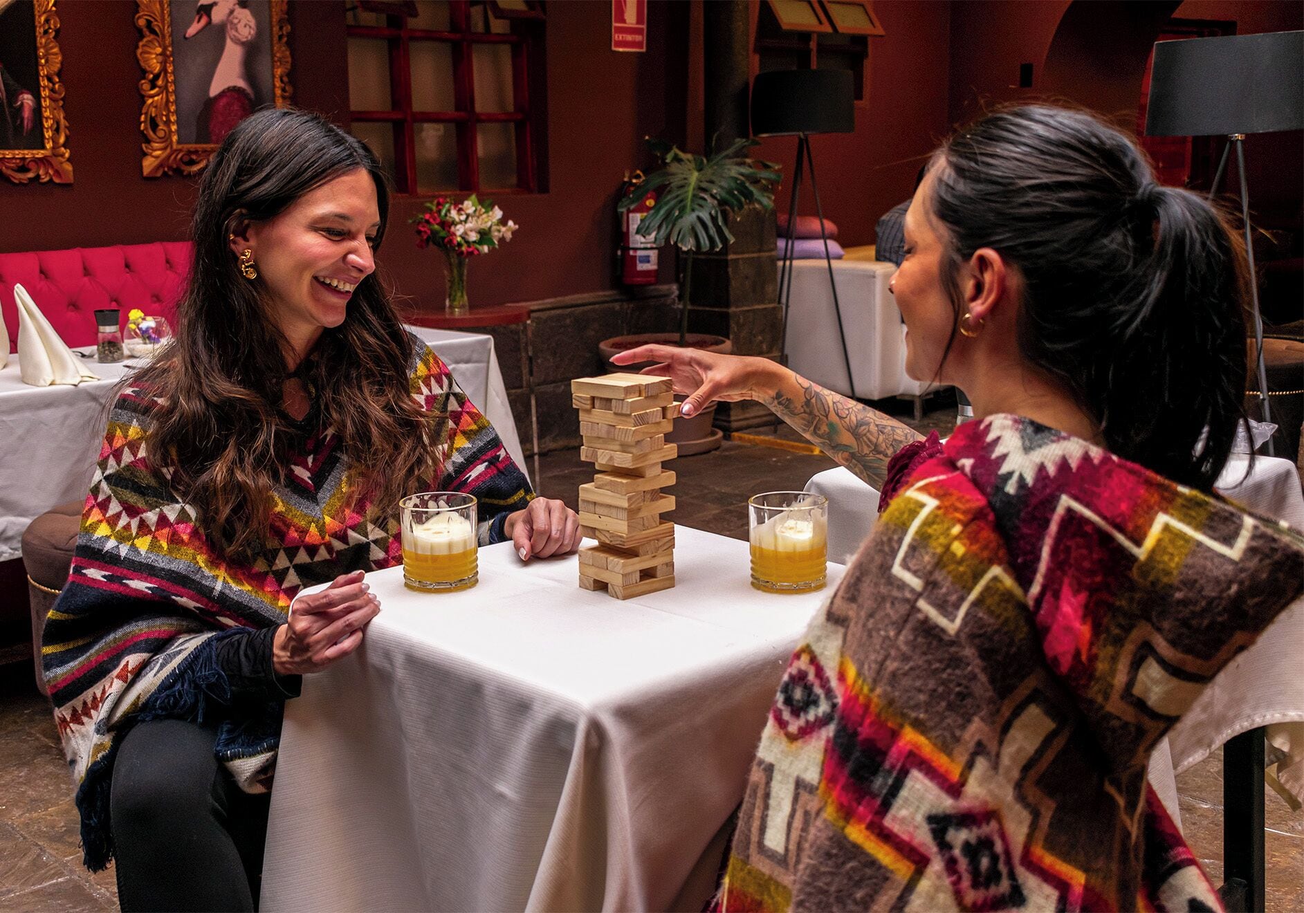 Dos personas jugando un juego de bloques de madera en una mesa, con vasos de cerveza.