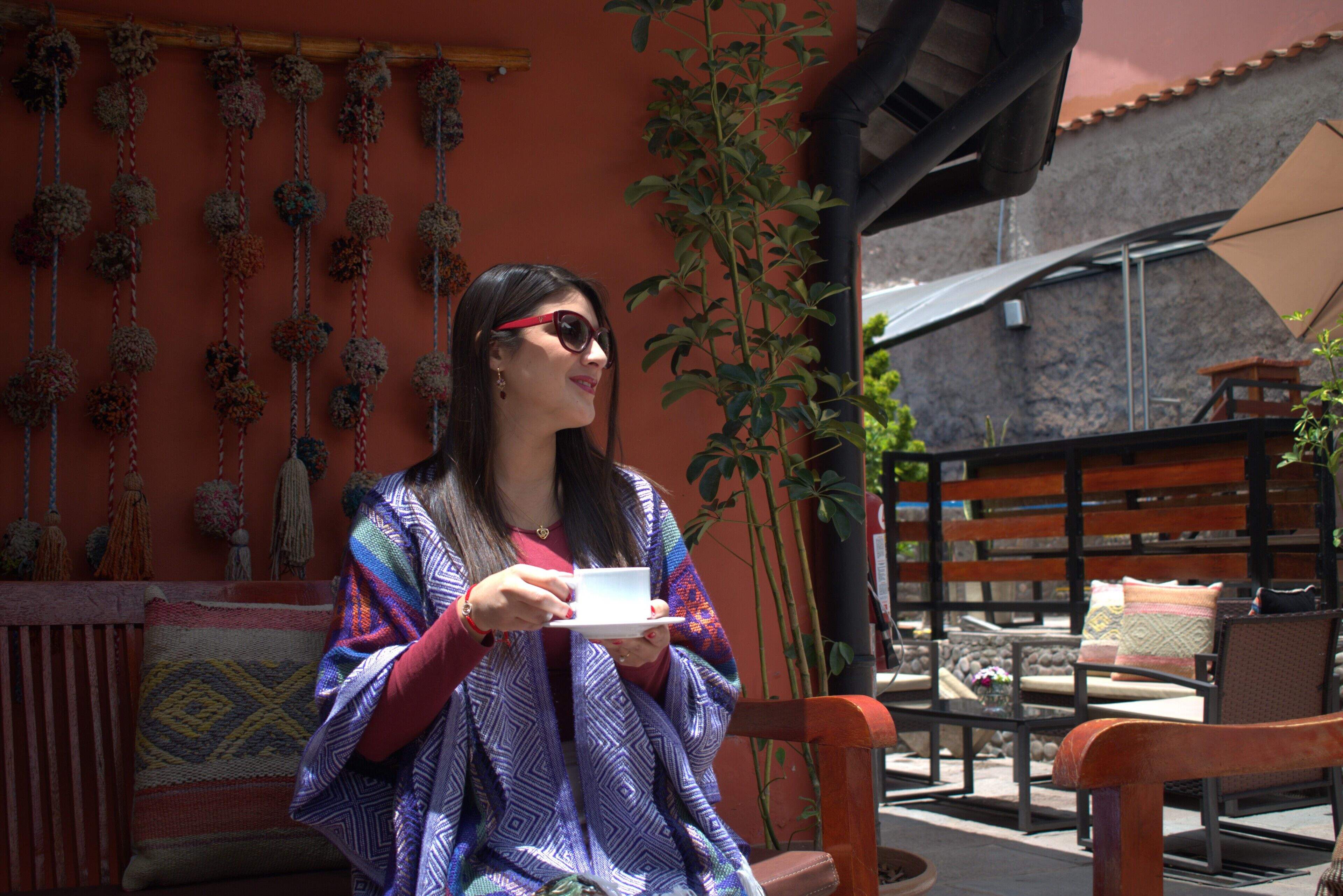 A person sitting on a wooden bench outdoors, holding a cup.