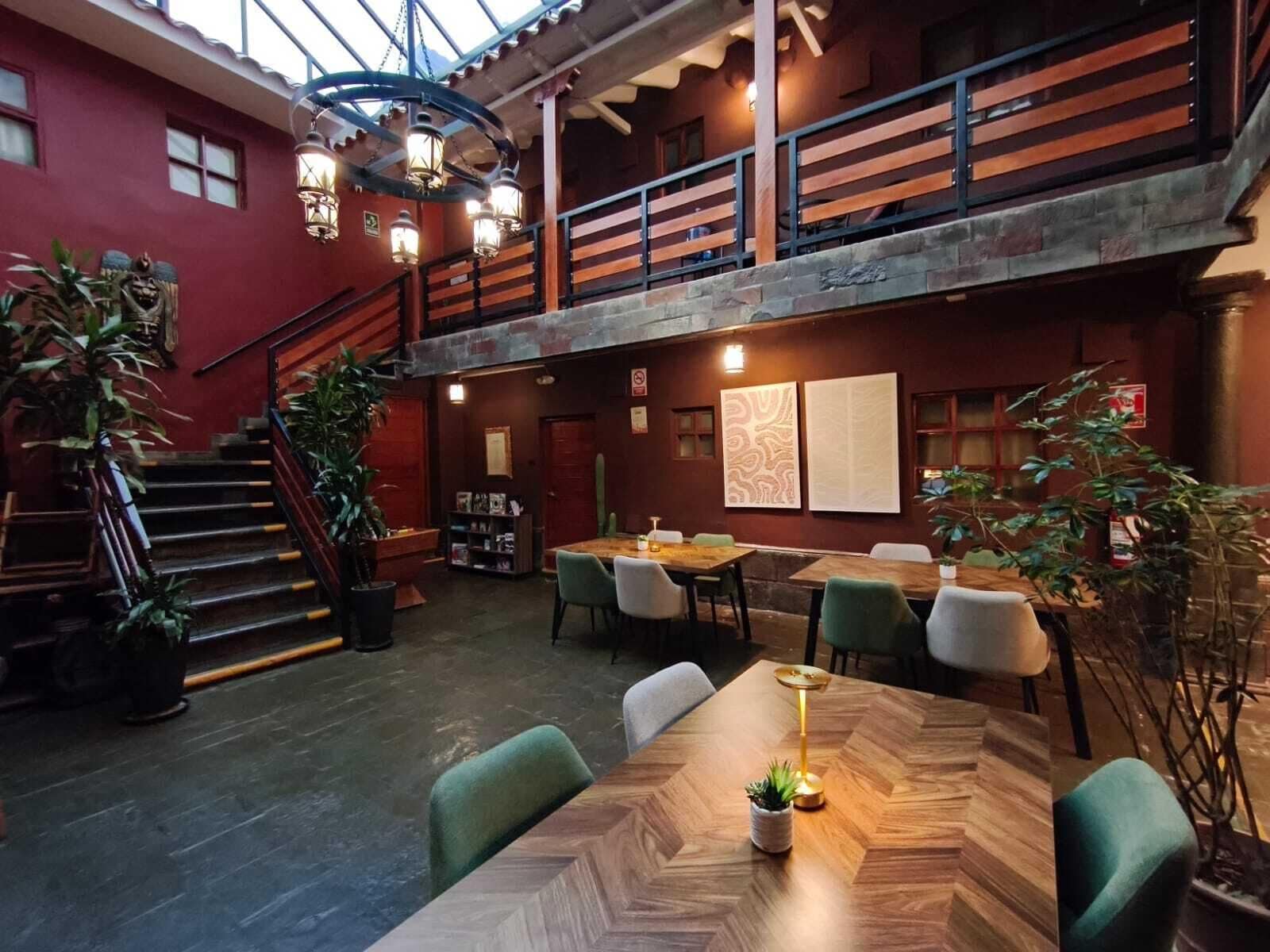 A restaurant with a herringbone-patterned dining table, green upholstered chairs, and a staircase leading to an upper level.