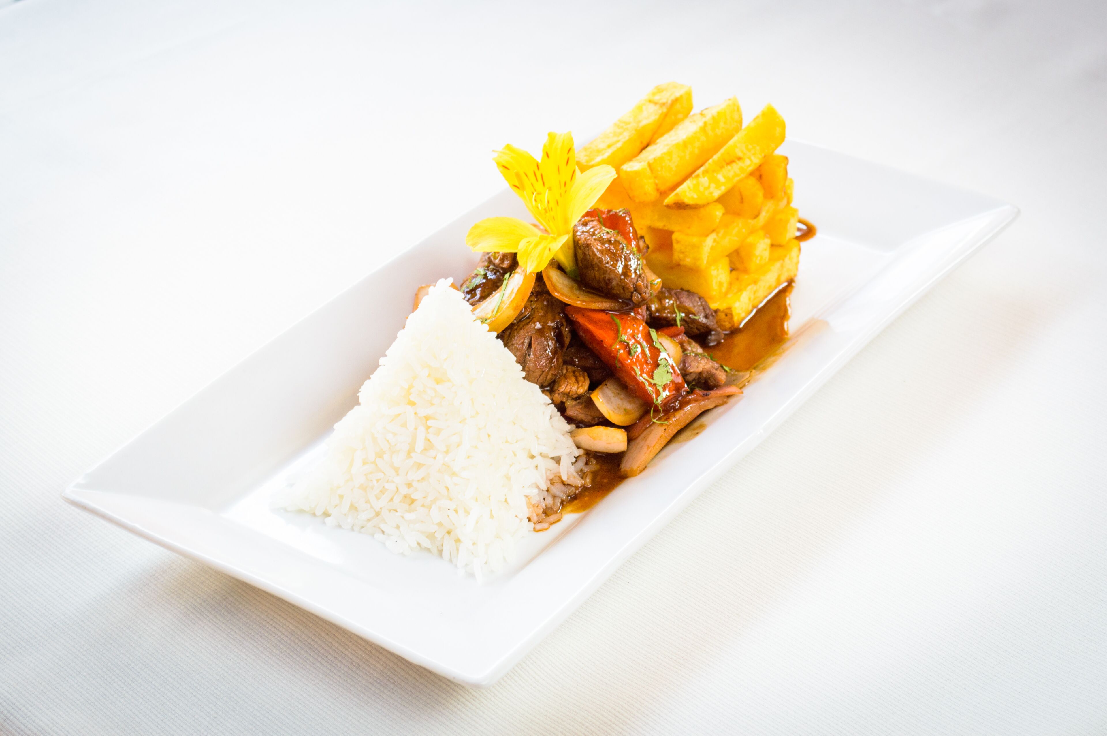 A white rectangular plate with white rice, a meat dish with vegetables, and French fries.