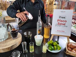 A bartender preparing a drink with a sign advertising a free Pisco Sour Master Class.