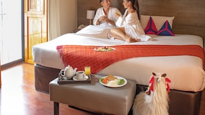 Habitación de hotel con una cama grande, techo de madera, ventana con cortinas y una pequeña mesa con alimentos para el desayuno.