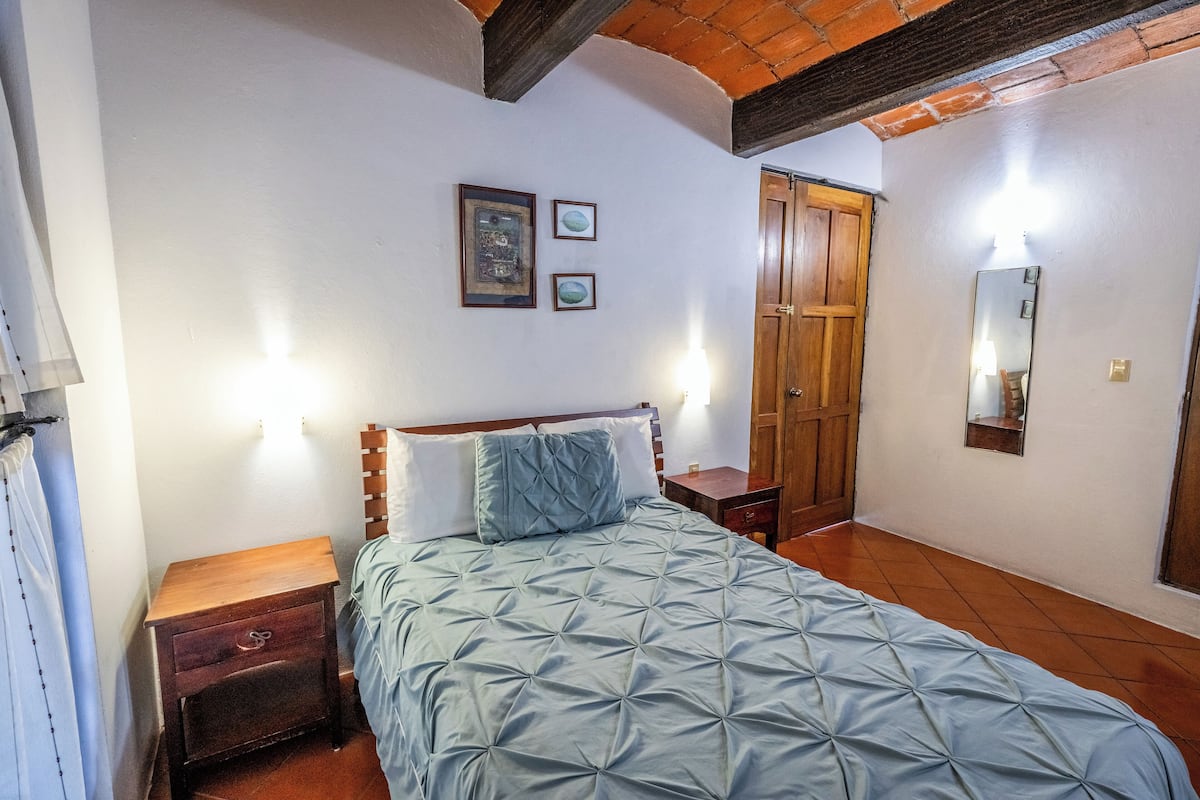 A bedroom with a bed, wooden nightstands, a wardrobe, and a mirror on the wall.