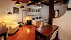 Un dormitorio con cama, escritorio, silla, lámpara y obras de arte en la pared.