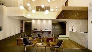 A modern reception area with a central desk, multiple seating arrangements, and a high ceiling with hanging lights. - Hotel Horizon and Convention Center (Morelia)