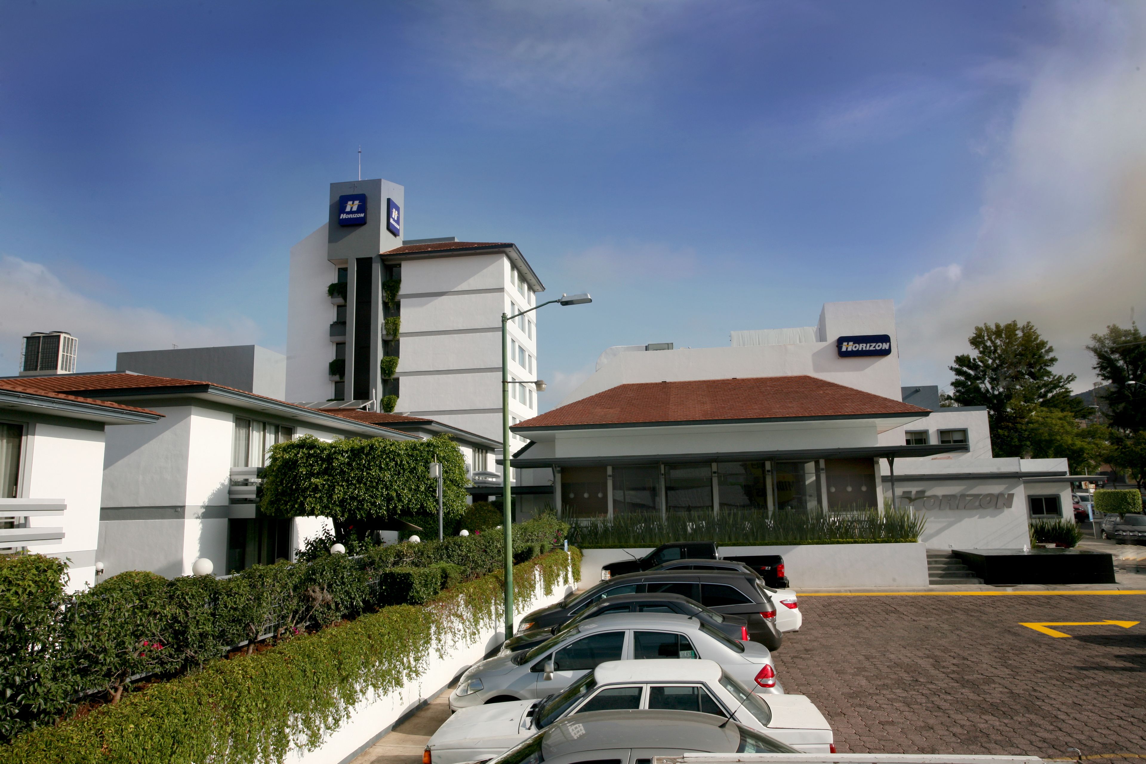 A parking lot with several cars, a Horizon building, and a white building with a red roof.