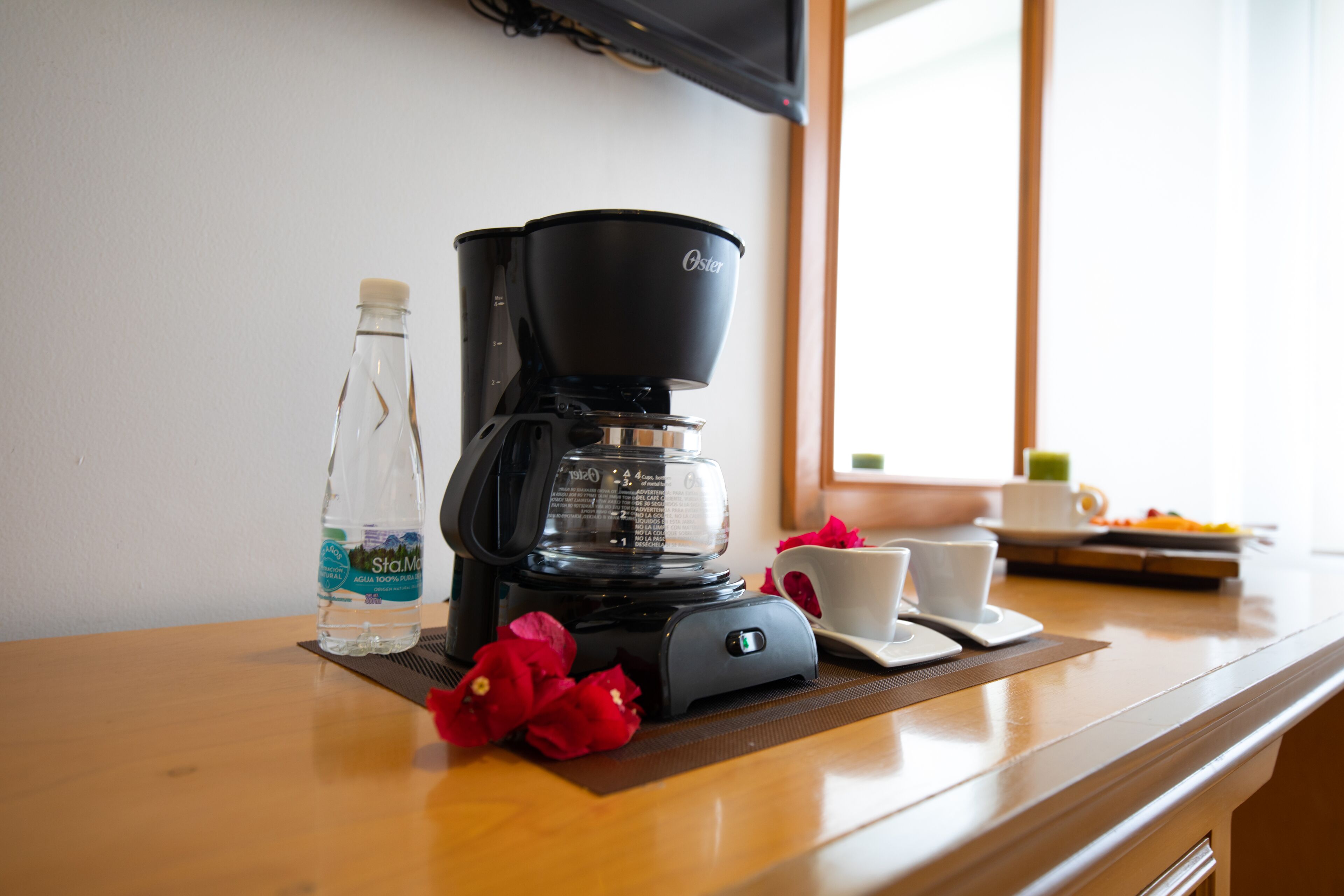 A coffee maker, a water bottle, and a cup on a wooden table.
