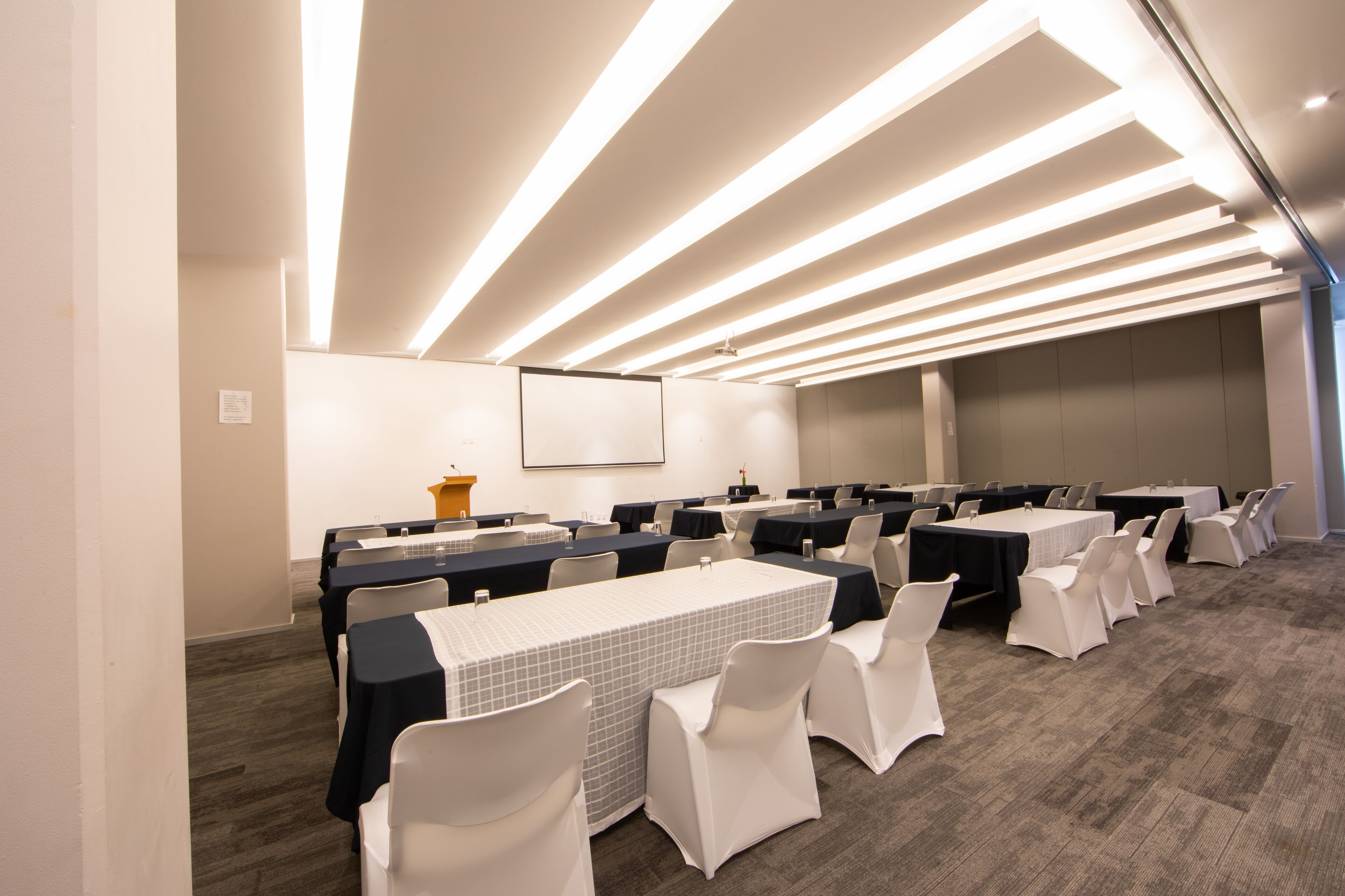 A conference room with tables and chairs, a podium, and a projector screen.