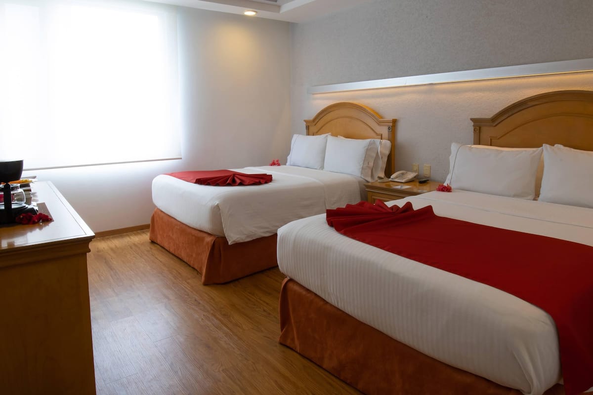 A hotel room with two beds, a desk with a phone, and a window.