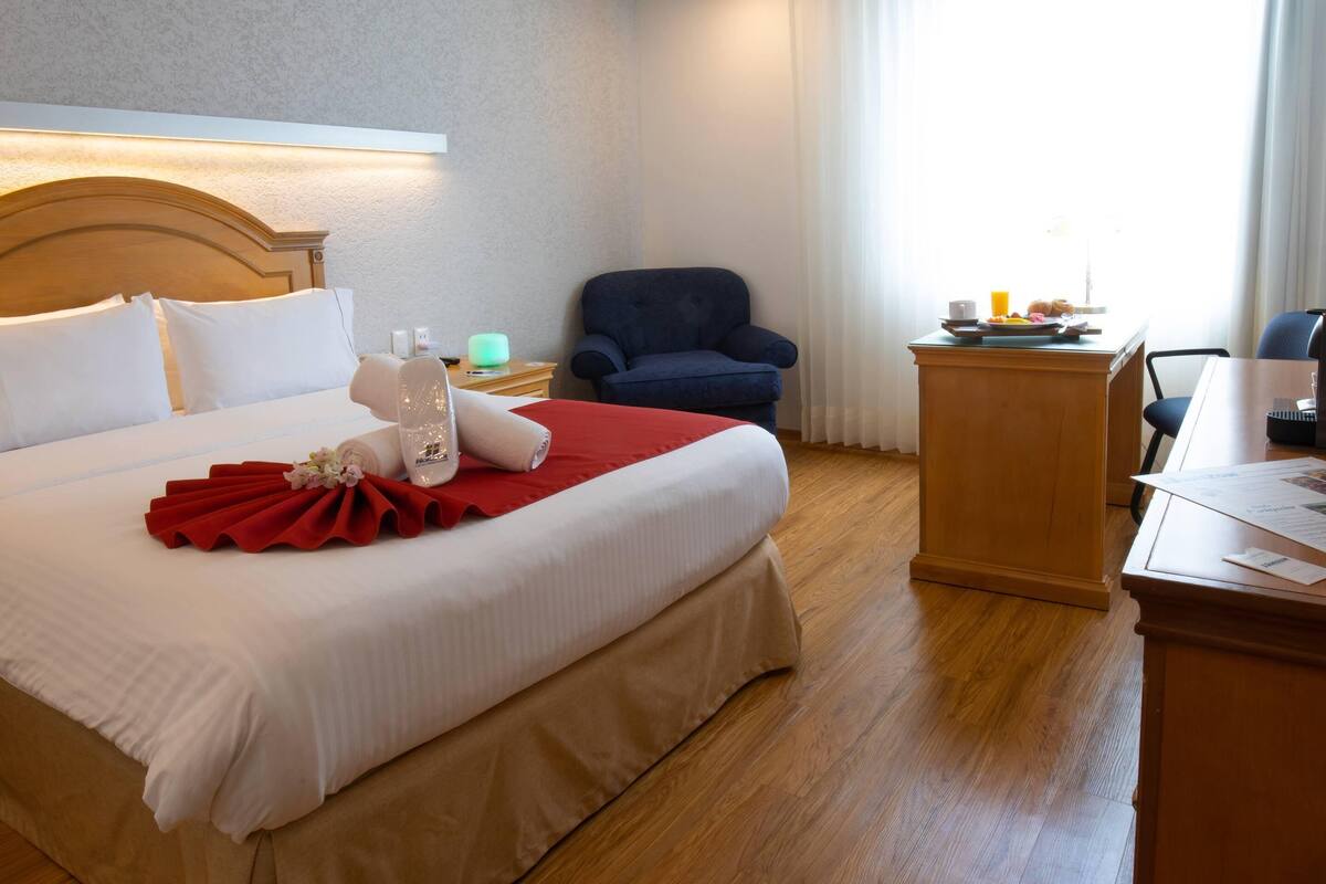 A hotel room with a bed, a desk, a chair, and a window with curtains.