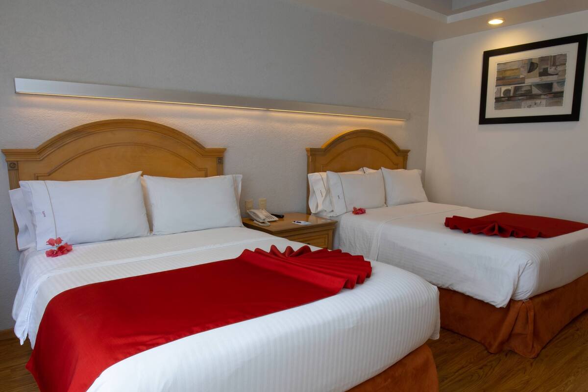 A hotel room with two beds, each with white bedding and red accents, wooden headboards, and a framed picture on the wall.